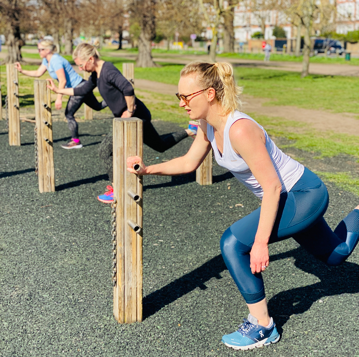 Group of mums performing Bulgarian lunges during outdoor fitness class in Clapham Common