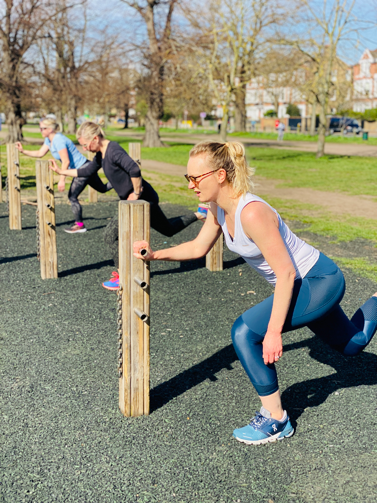 Group of mums performing Bulgarian lunges during outdoor fitness class in Clapham Common