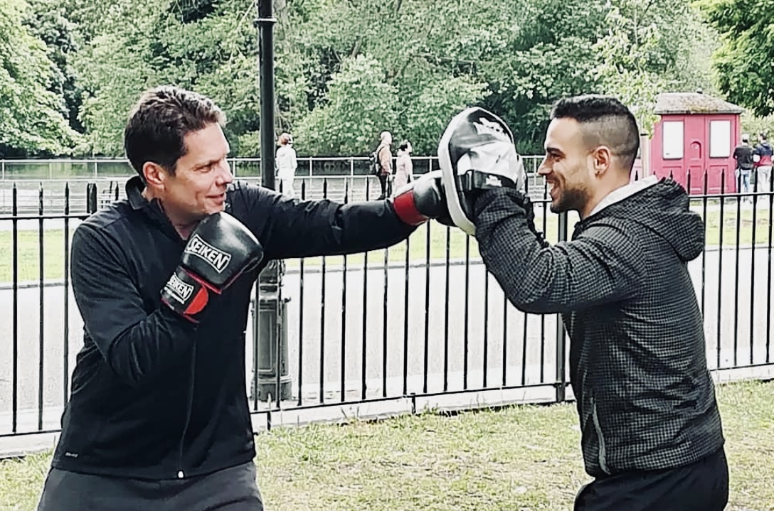 Personal trainer leading boxing session with client in Battersea Park near the lake