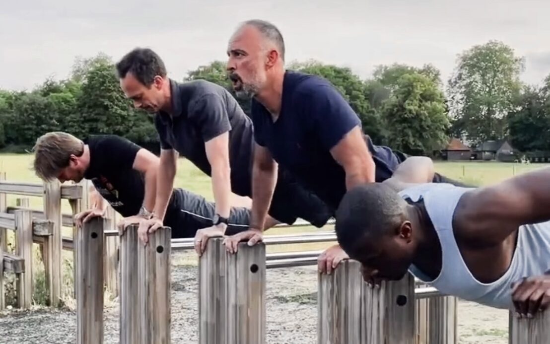 Outdoor bootcamp in Clapham Common with four men doing push-ups on outdoor gym bars