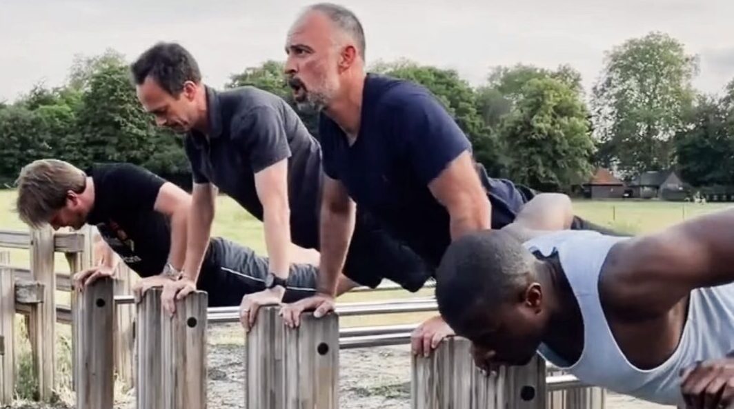 Outdoor bootcamp in Clapham Common with four men doing push-ups on outdoor gym bars